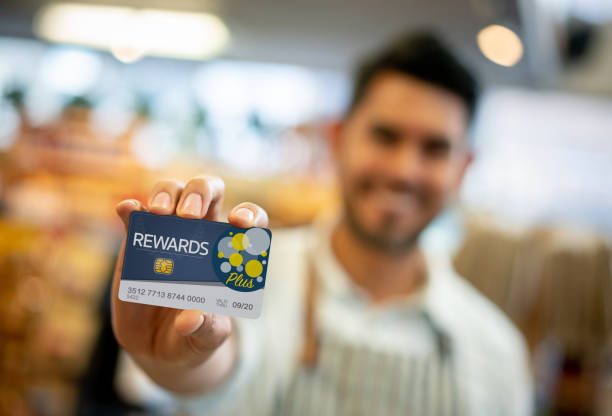 Salesman at a grocery store holding a loyalty program card up front - Focus on foreground **DESIGN ON CARD WAS MADE FROM SCRATCH BY US**
